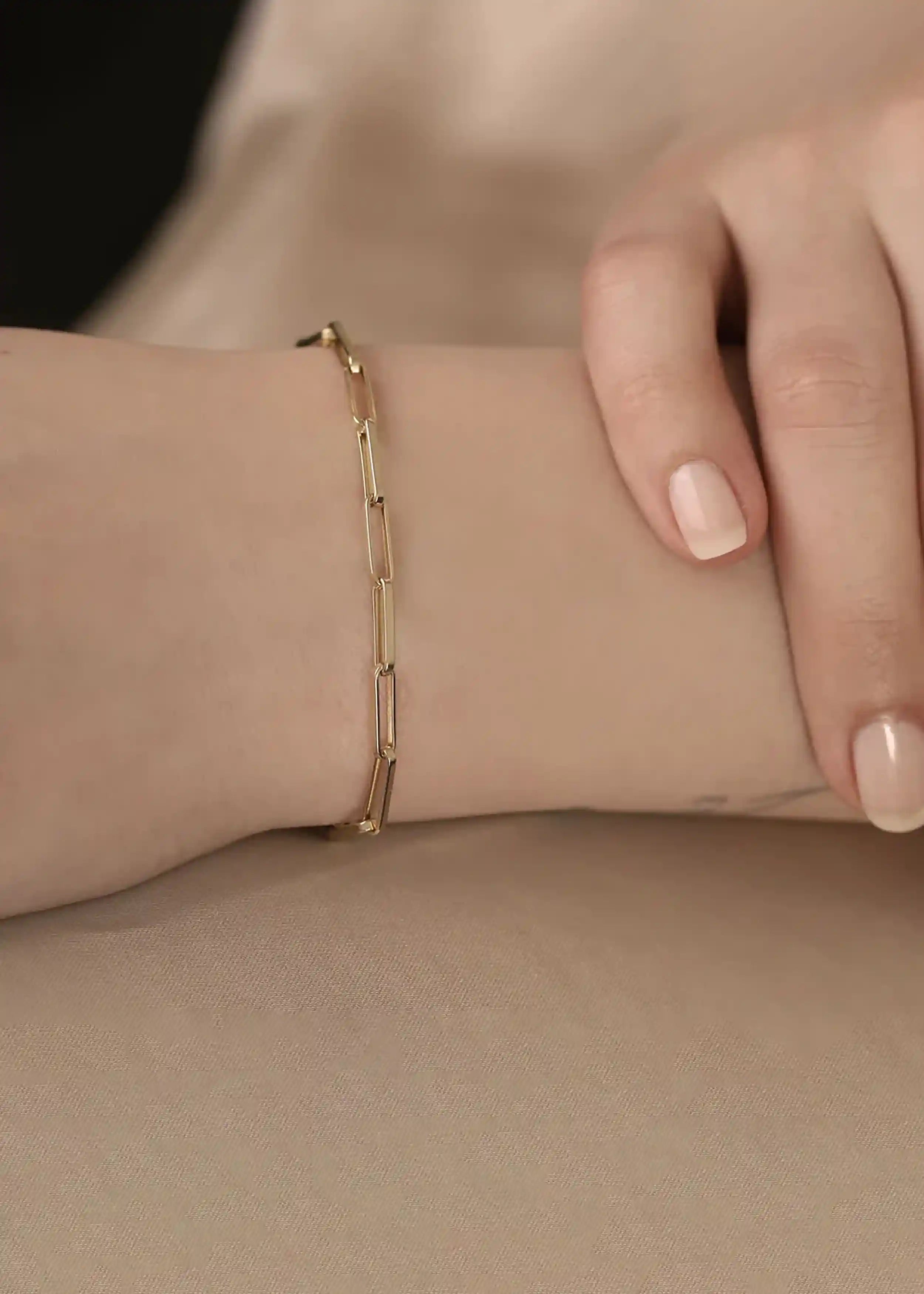 Das Armband hat ein modernes, minimalistisches Design mit einer Paperclip-Kette, die aus flachen, rechteckigen Gliedern besteht, die an Büroklammern erinnern – ein beliebter Trend in der zeitgenössischen Schmuckgestaltung.