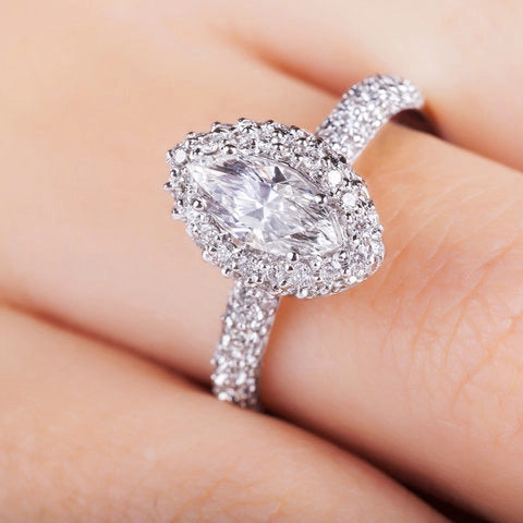 Nahaufnahme einer Hand mit einem eleganten Verlobungsring von Anadolu Juweliere, der einen marquise-geschliffenen Diamanten mit einem Halo aus kleineren Diamanten zeigt, luxuriösen Schmuck in Düsseldorf hervorhebend.