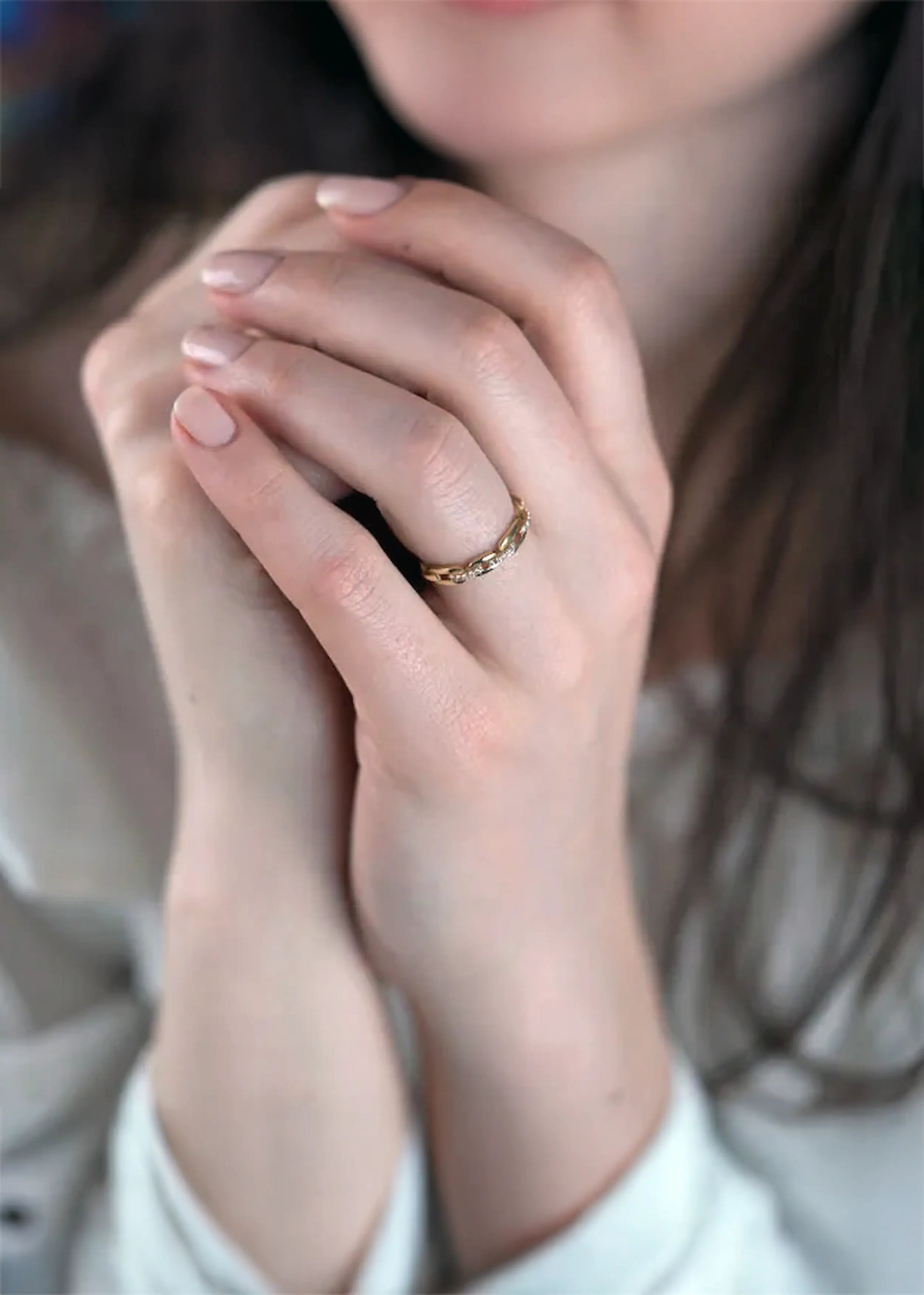Goldener 14-Karat-Ring mit Kette-Design und funkelnden Steinen, am Finger einer Person. Die Person trägt ein weißes Kleidungsstück und hat naturfarbene Nägel.