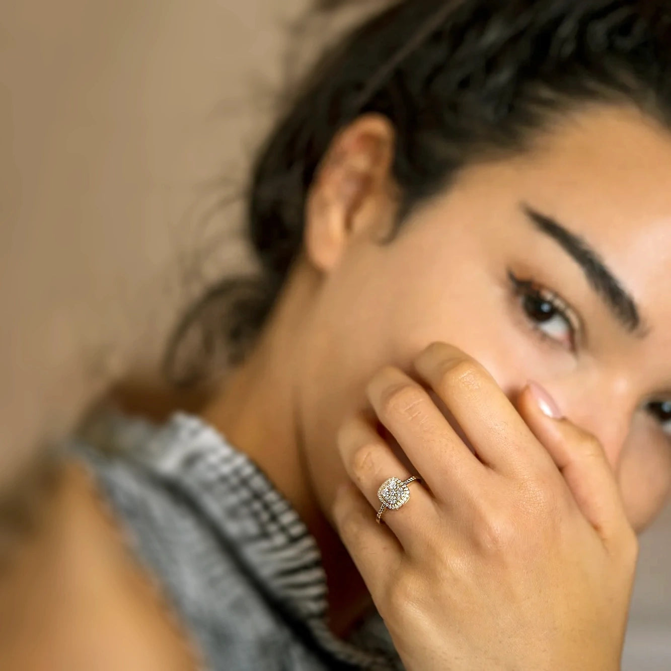 Nahaufnahme einer Frau mit dunklem Haar, die einen eleganten Verlobungsring mit einem runden Edelstein und einem Halo aus kleineren Diamanten von Anadolu Juweliere trägt, in einer nachdenklichen Pose, die luxuriösen Schmuck in Düsseldorf hervorhebt.