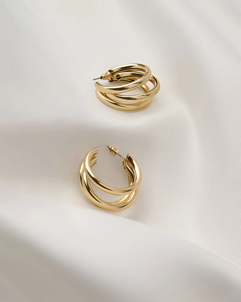 Zwei Paar minimalistische Gold-Creolen-Ohrringe mit ineinandergreifendem Design von Anadolu Juweliere, elegant auf weißem Stoff präsentiert, die schlichte Handwerkskunst in Düsseldorf hervorhebend.