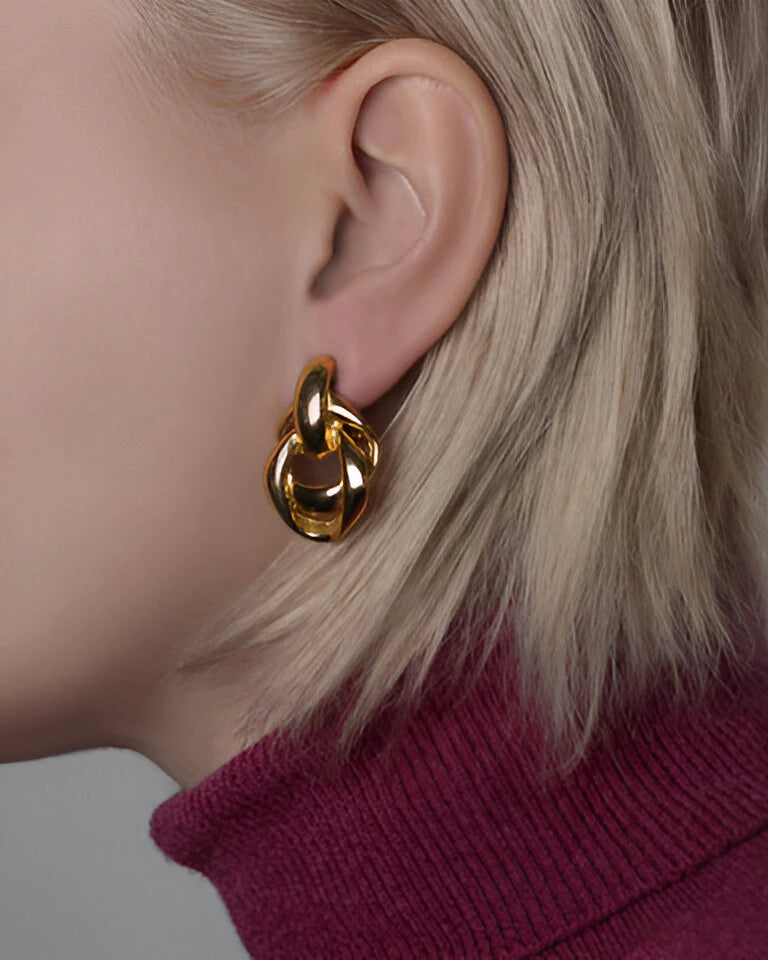 Nahaufnahme einer stilvollen Frau mit platinblondem Haar, die einen auffälligen, ineinandergreifenden Gold-Creolen-Ohrring von Anadolu Juweliere trägt, und die elegante Handwerkskunst von Schmuck in Düsseldorf präsentiert.